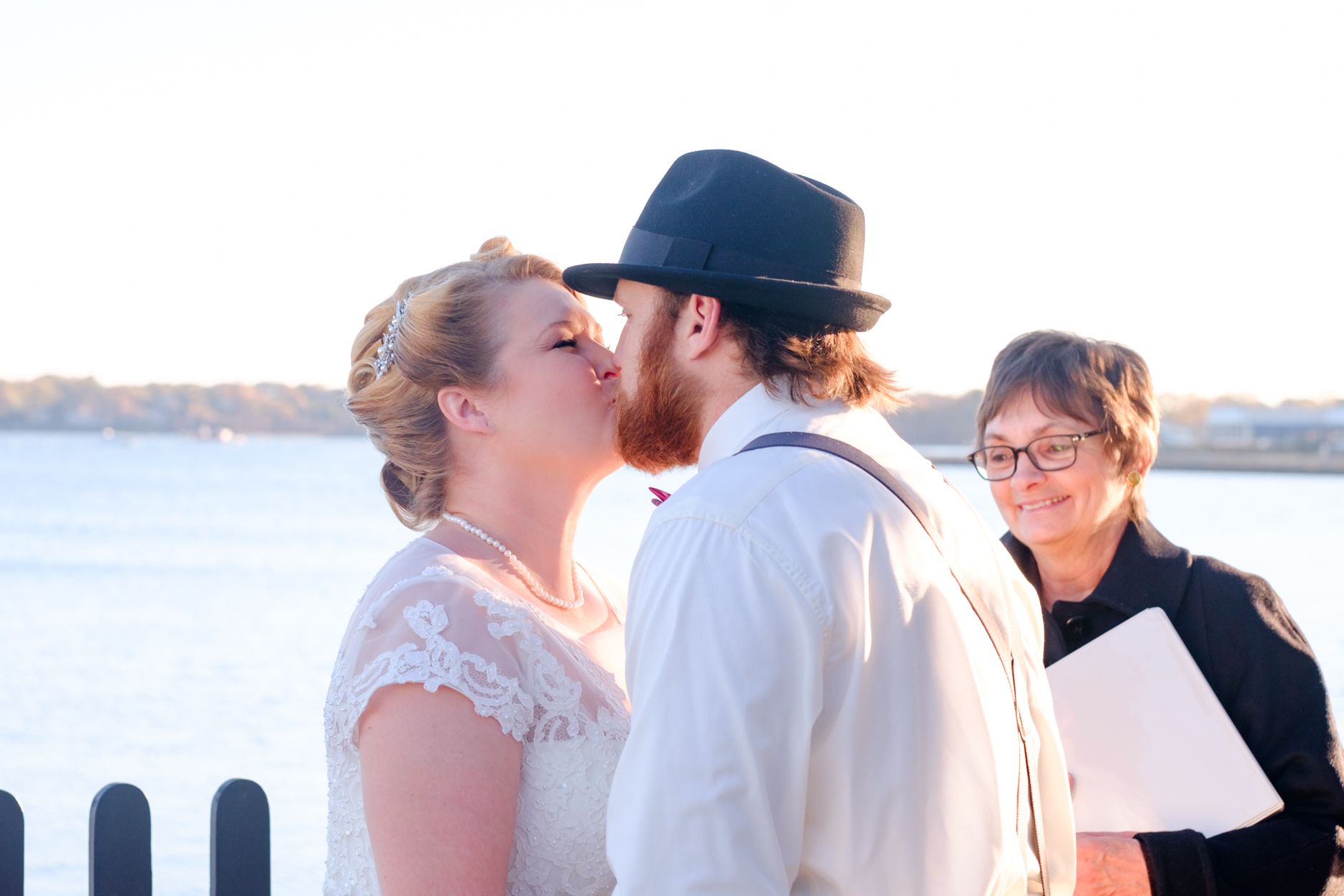 Bride and groom kiss as the get married in the historic house of the seven gables in salem massachusetts. This elopement has a classic pin up style with a tea length dress, red and black accents, a bow tie, a fedora, and gorgeous curls in her hair. This North Shore elopement was an intimate wedding and it was an honor to be the photographer for this couple.