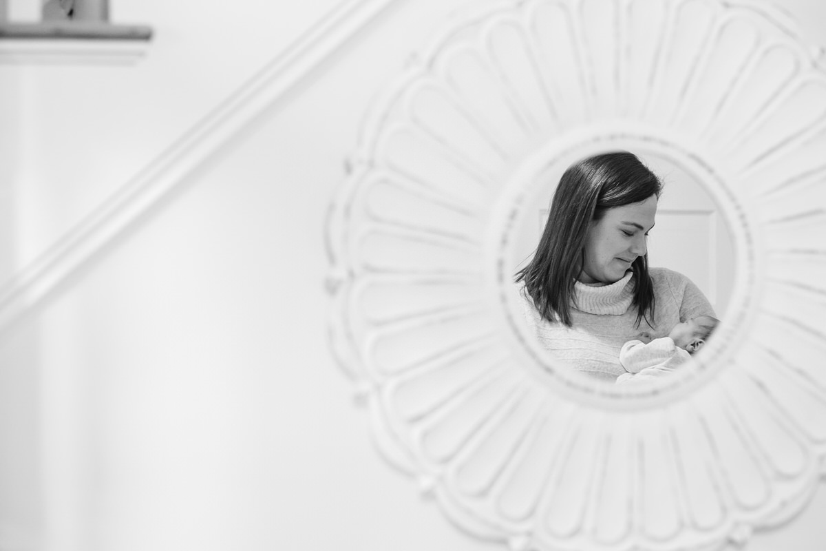 Newborn baby girl held by mom, reflected in a flower-like mirror.