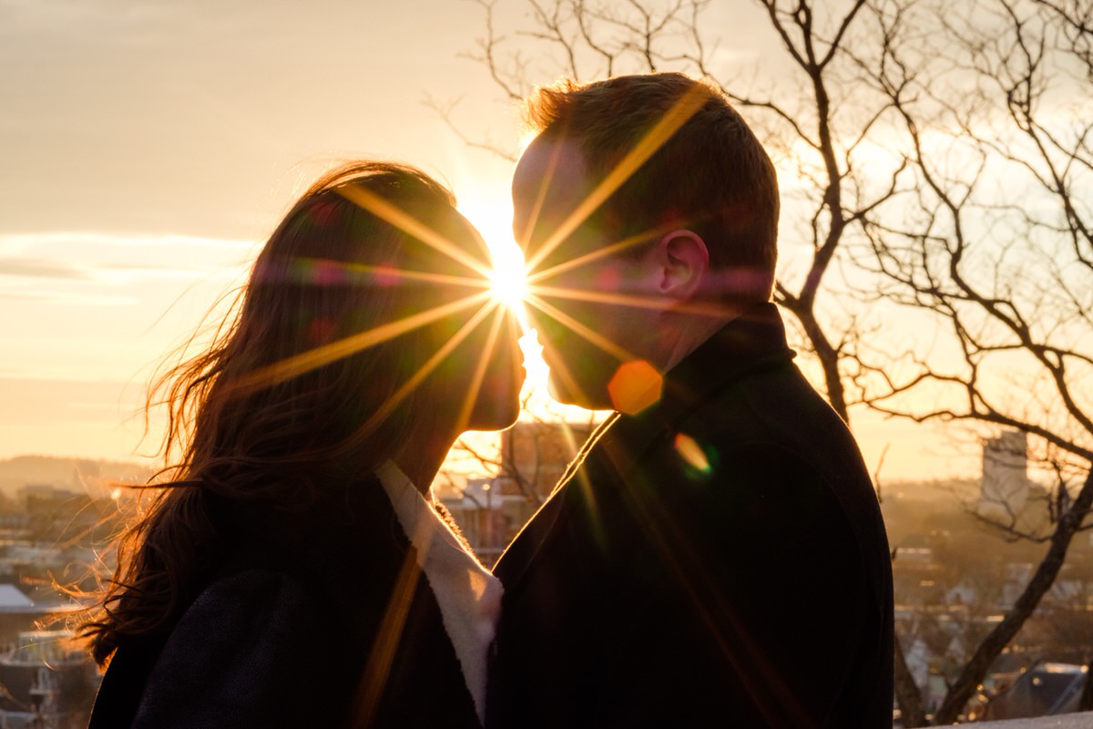 Engaged couple nuzzling with a sun flare in winter in Prospect Hill Park