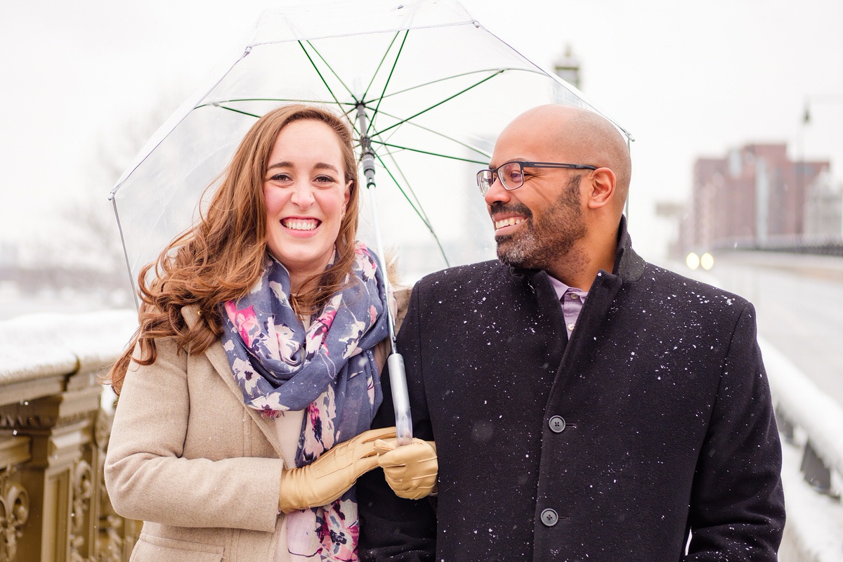 Engaged couple walks on the Longfellow Bridge on a snowy winter afternoon in Boston.