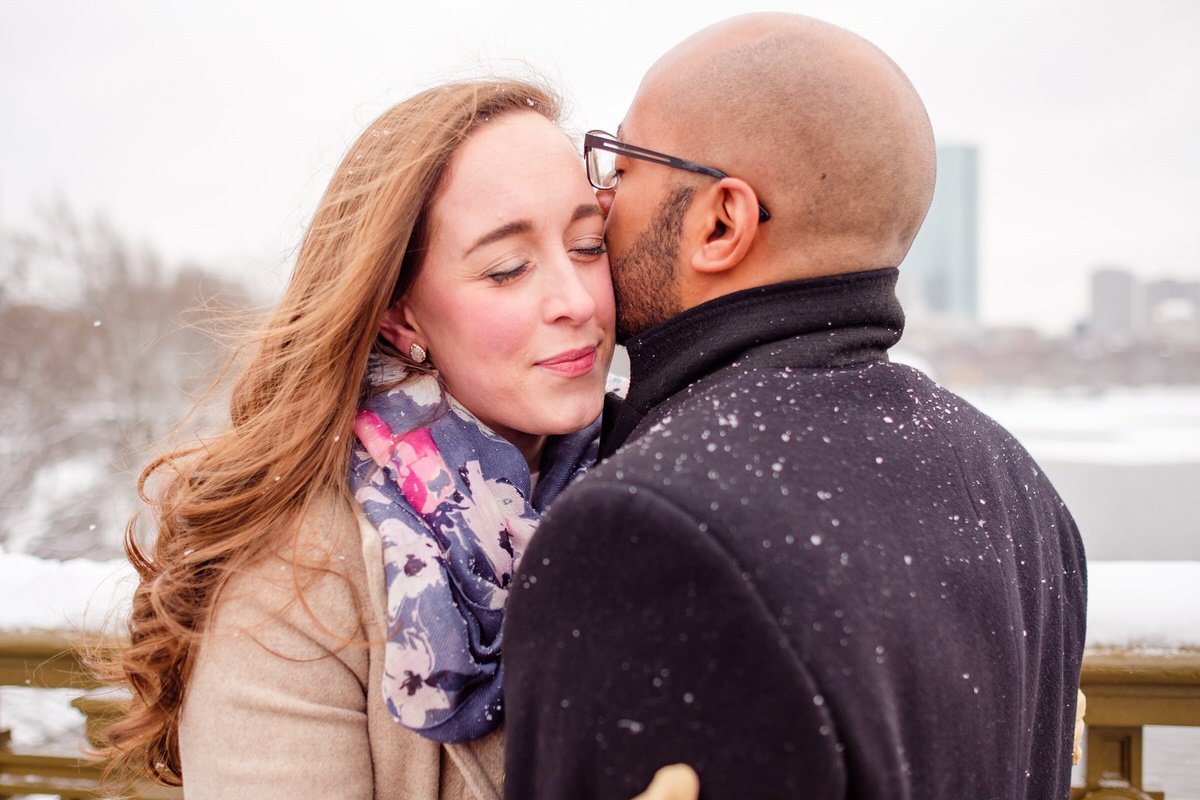 Engaged couple embraces on the Longfellow Bridge on a snowy winter afternoon in Boston.