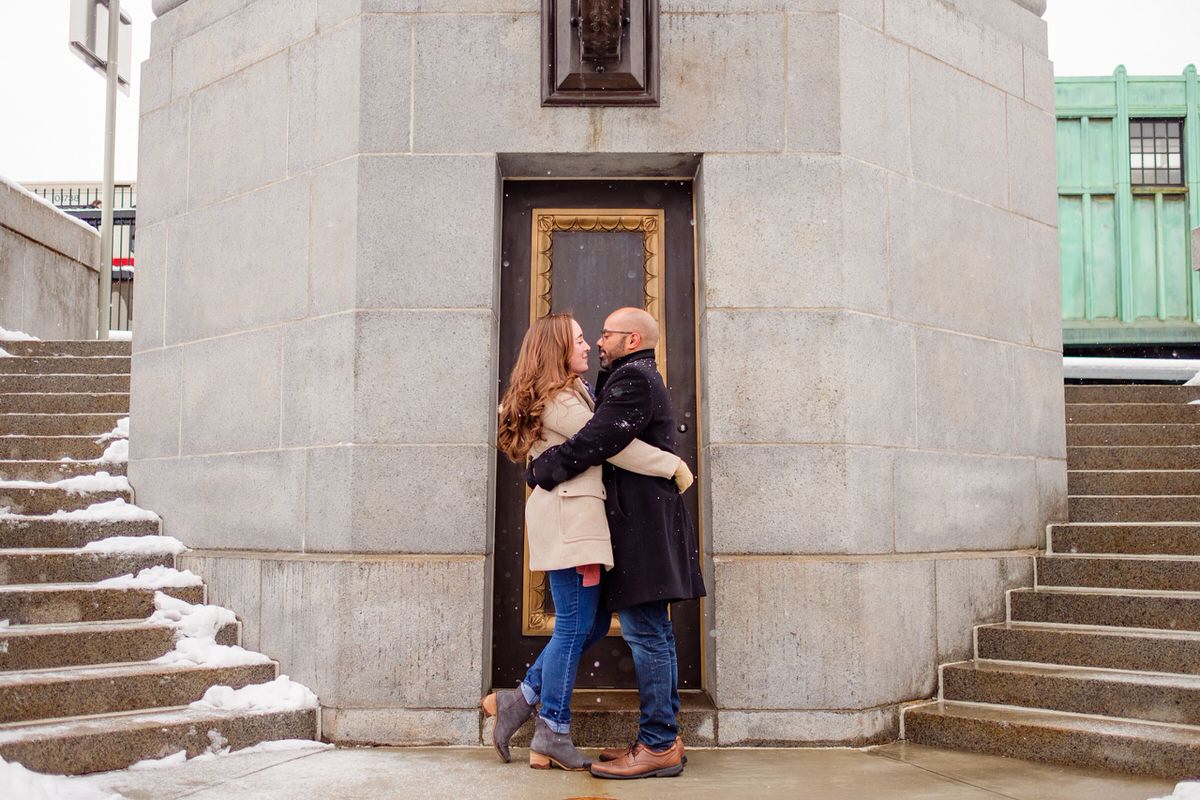 Engaged couple embraces on the steps of the Longfellow Bridge in front of the Charles MGH red line T stop in Boston.