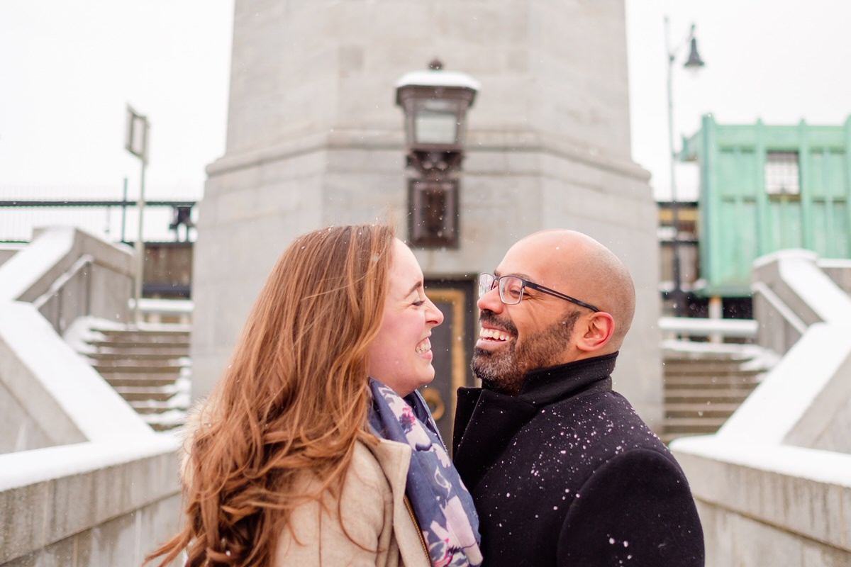 Engaged couple laughs on the steps of the Longfellow Bridge in front of the Charles MGH red line T stop in Boston.