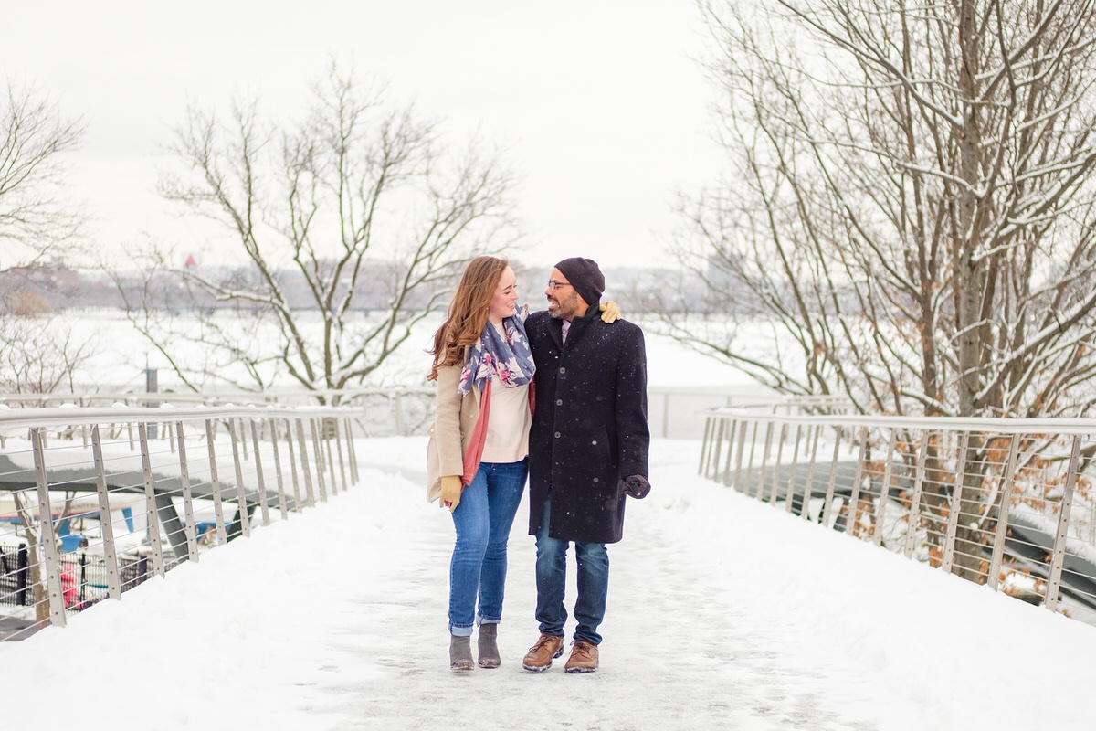 Engaged couple walks on a pedestrian bridge near the Charles River Esplanade in Boston on a snowy afternoon in winter.