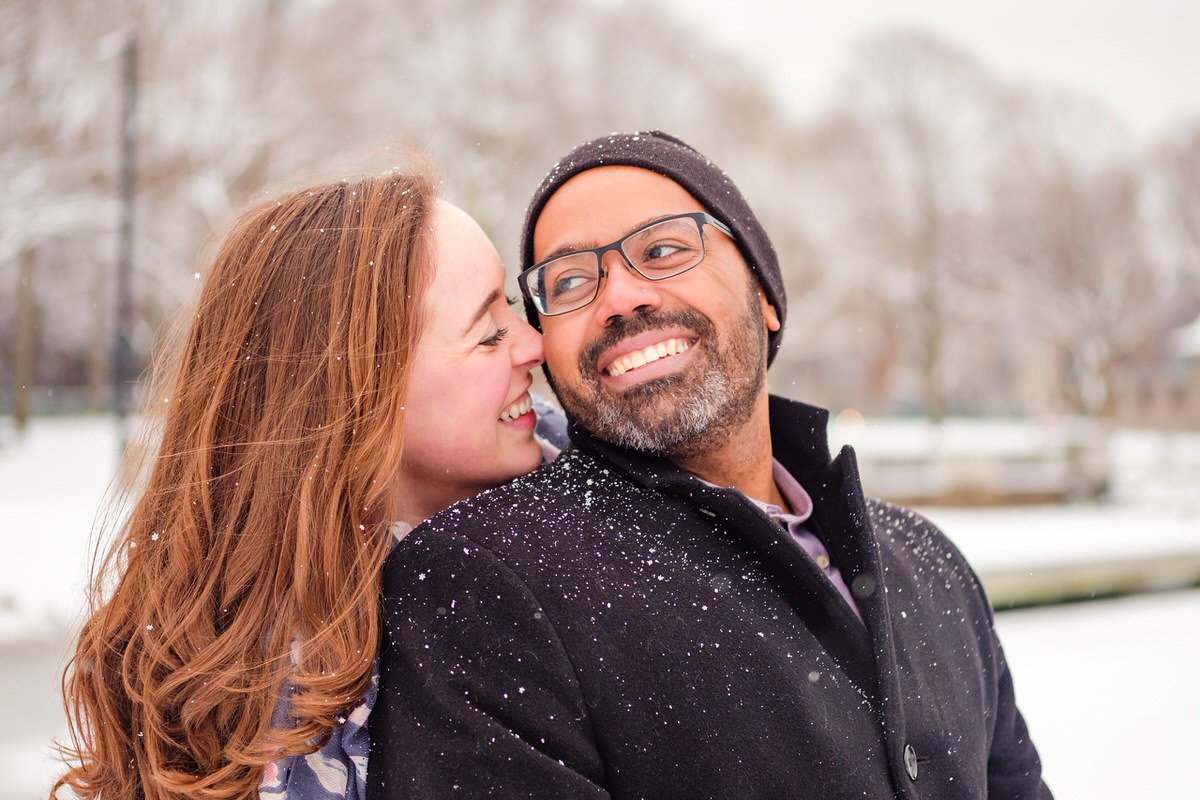 Engaged couple snuggles on a snowy winter day on the Charles River Esplanade in Boston