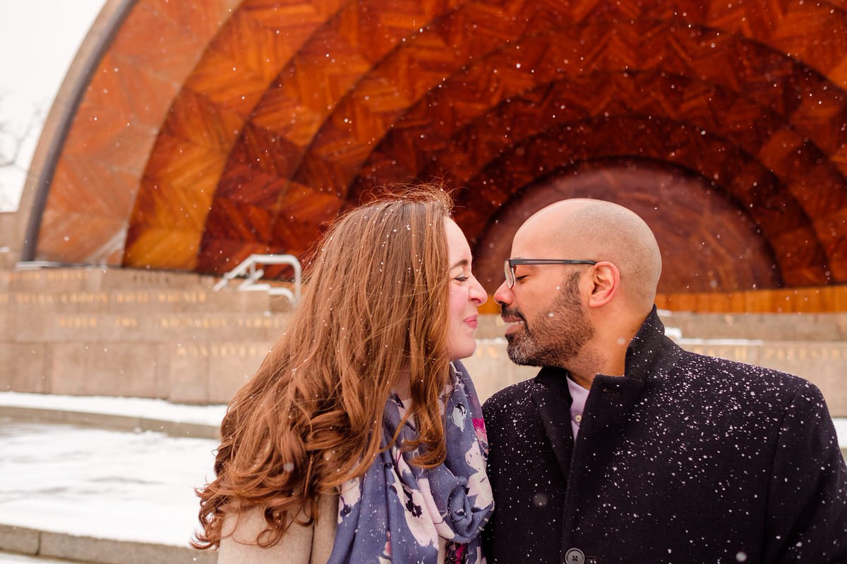 Engaged couple nuzzles in front of the Hatch Shell on the Charles River Esplanade in Boston.