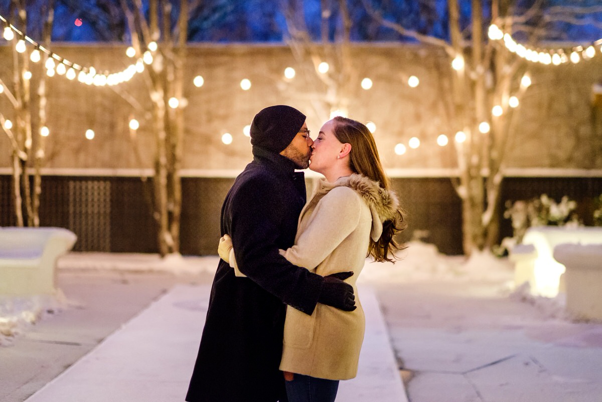 Engaged couple kisses in the courtyard of the Liberty Hotel on a snowy evening in Boston.