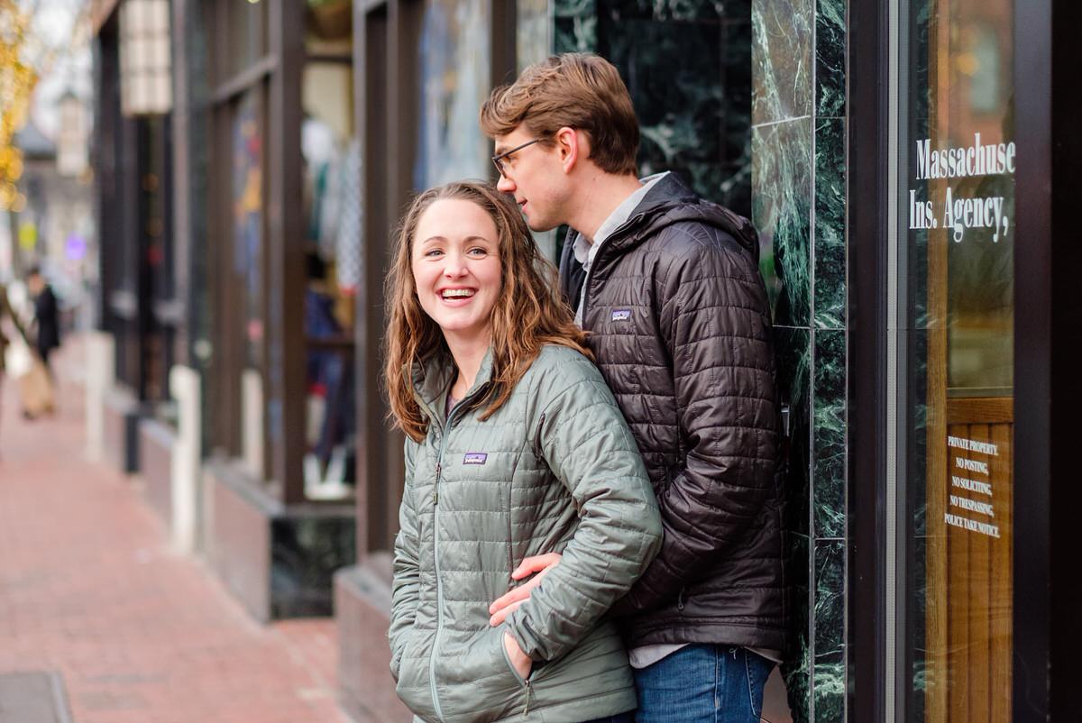 Couple hug in front of stores in a winter engagement session in Davis Square