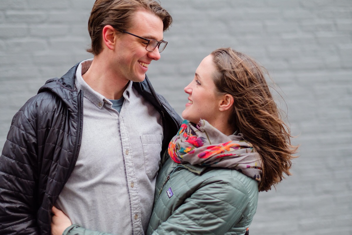 Engaged partners pose in front of a grey wall during a winter engagement session in Somerville