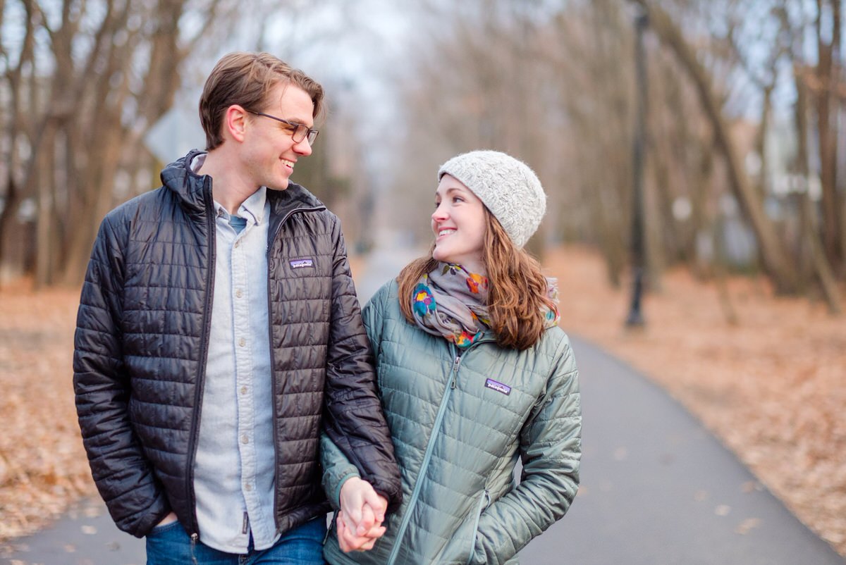 Engaged couple in Patagonia coats walks down the Davis Square bike path during a winter engagement photo session