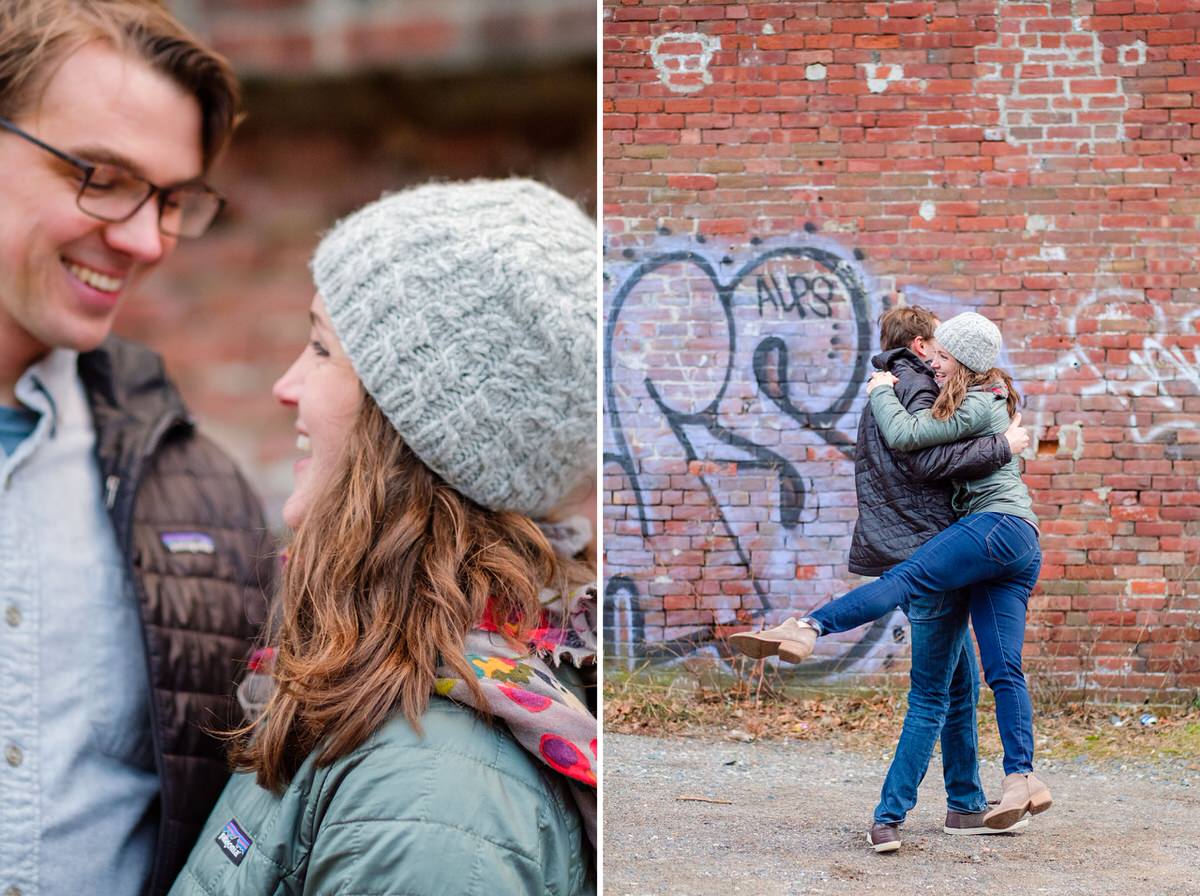 Engaged couple smiles and spins in front of a brick graffitied wall in Boston