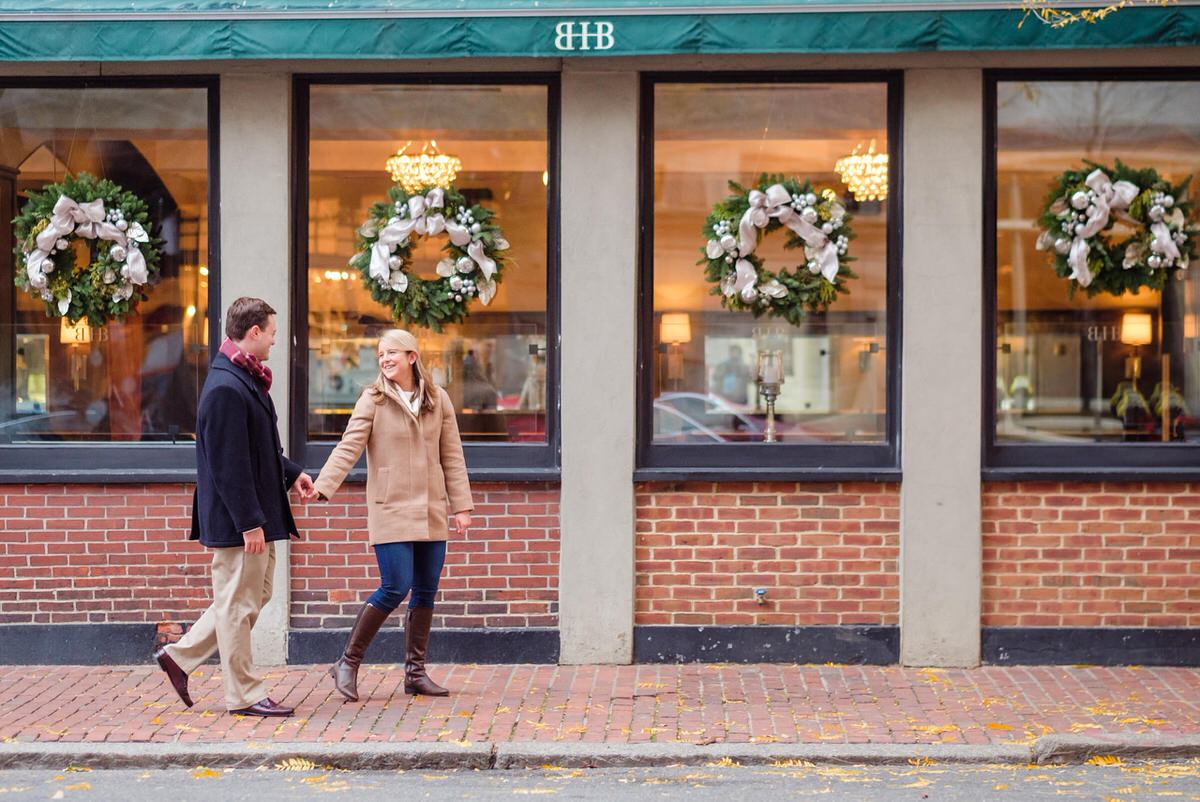 Engaged couple in winter coats stroll down a brick street in front of the Beacon Hill Hotel and Bistro