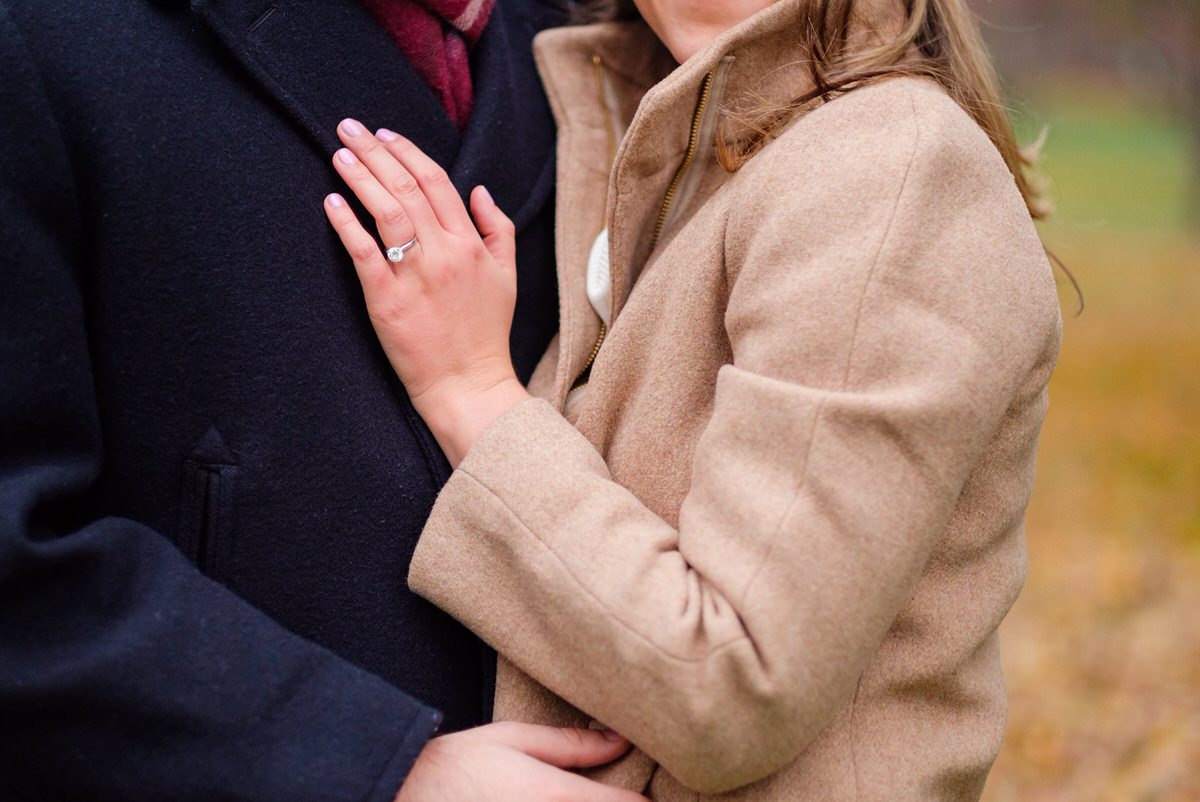 Engaged man in a black peacoat and his fiance in a camel coat hold each other in the Public Garden in downtown Boston during a fall engagement photo session