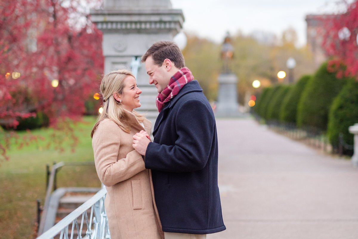 Engaged couple in winter coats dances on the Lagoon Bridge in the Public Garden in Boston