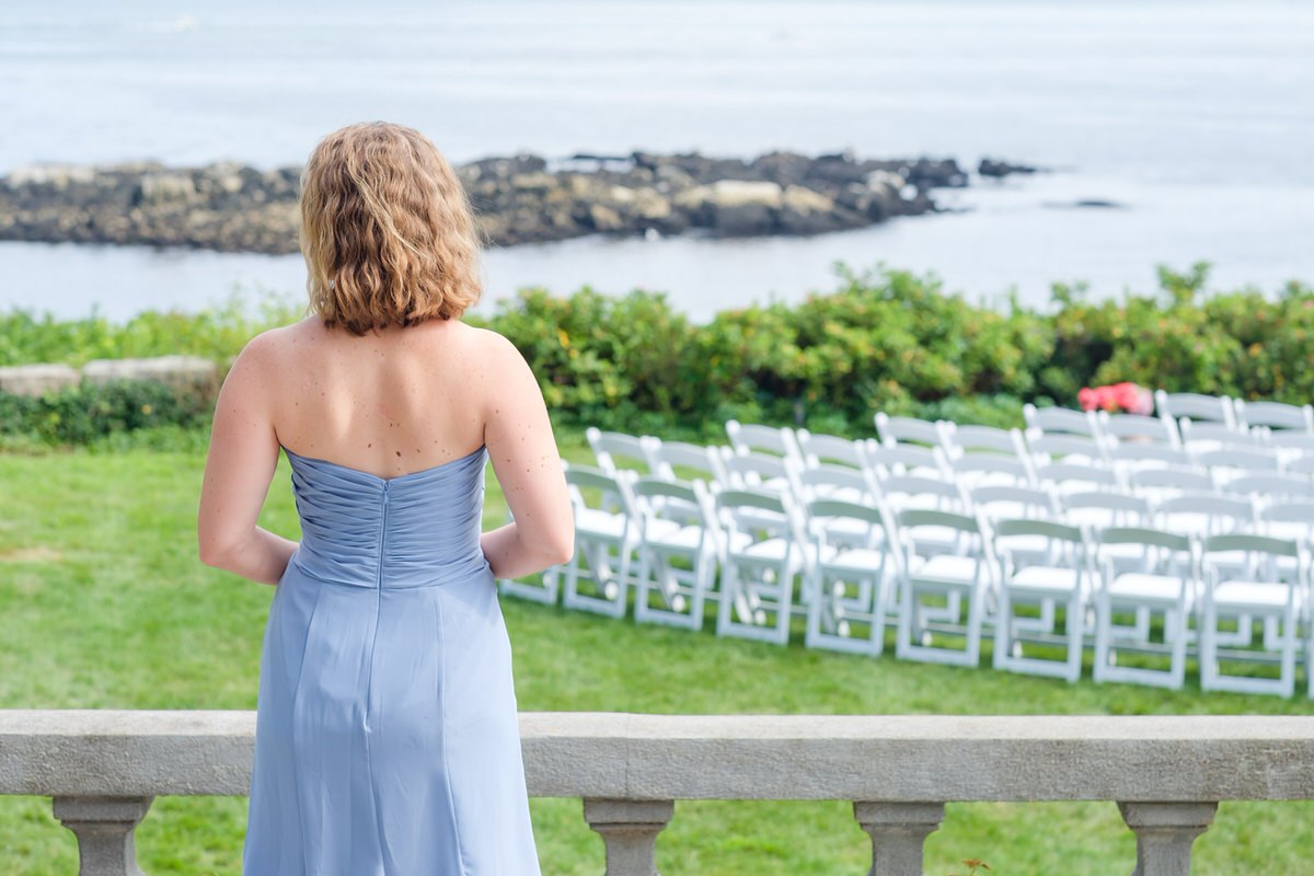 Flower girl in blue dress overlooks oceanside ceremony site at Misselwood manor in New England