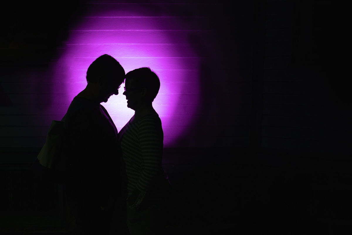 Lesbian couple in a purple halo of light snuggles in and artistic edgy engagement portrait