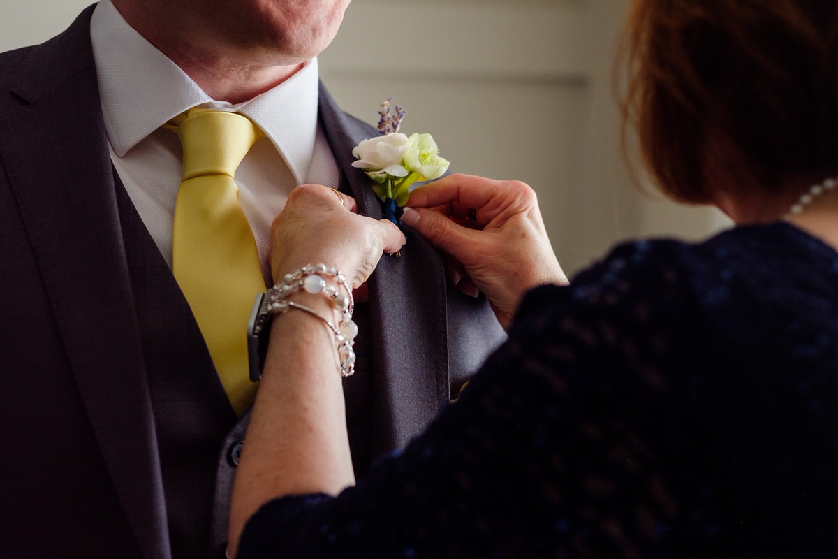 Close up of mom pinning on the groom's boutonniere before his wedding day