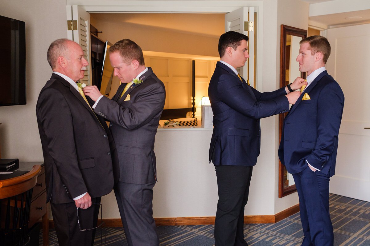 Groom pinning on his dad's boutonniere while groomsmen adjust their ties in the Charles Hotel in Harvard Square