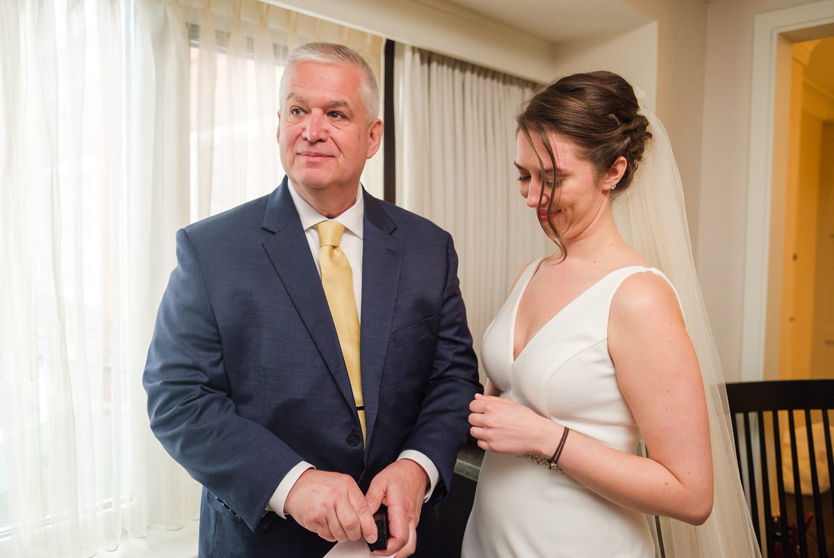 Bride holds her dad's arm as he opens a small wedding day gift