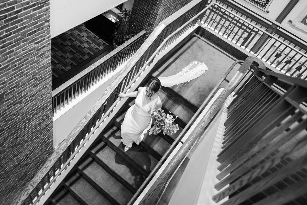 Bride with long flowered veil walks down stairs of the Charles Hotel in black and while