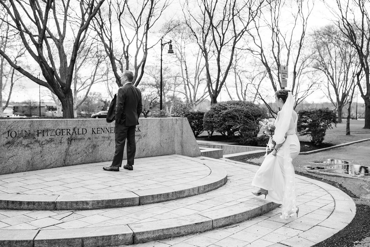 In black and white, bride approaches her groom in JFK Park in Cambridge, MA before her first look