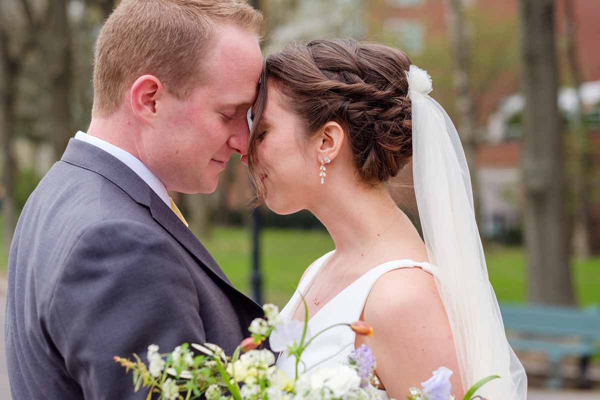 Bride in white and groom in grey suit snuggle in a park