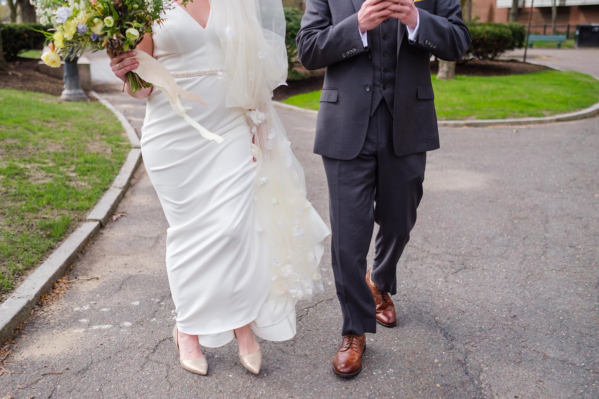 Bride's dress blows in the wind as groom in a grey suit checks his cell phone