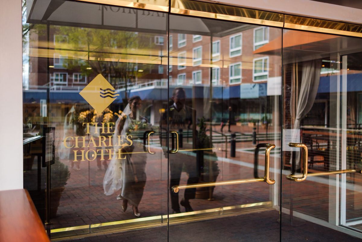 Bride and groom are reflected in the glass door of the Charles Hotel in Cambridge, MA