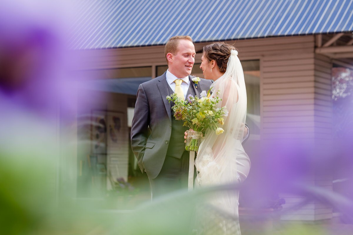 Bride and groom stand together with lavender flowers in the foreground 