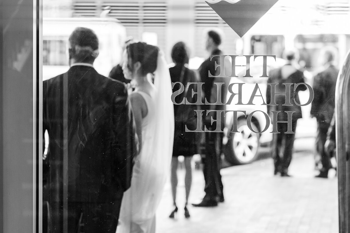 Bride and groom in black and white stand behind glass door of the Charles Hotel in Harvard Square