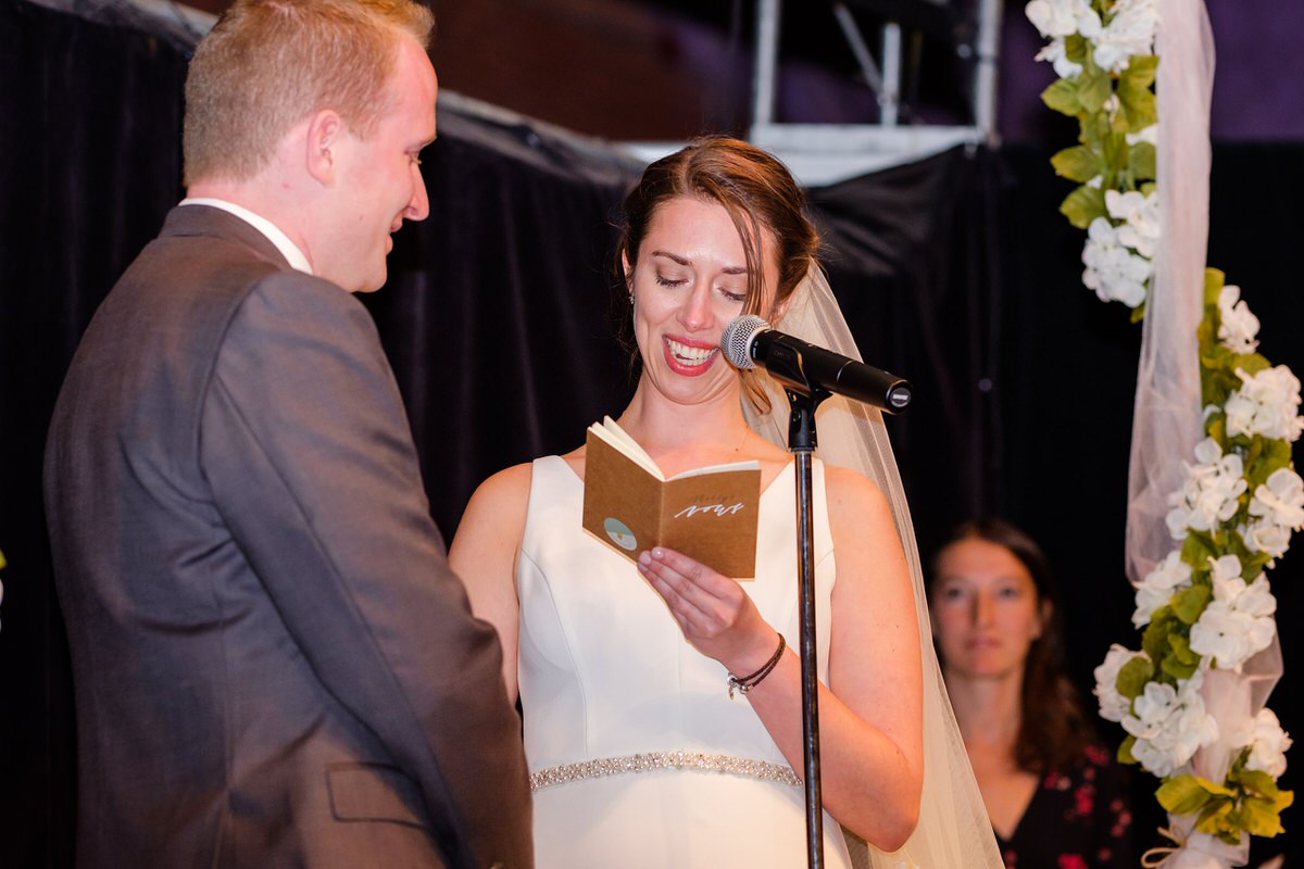 Bride reads vows to her groom from a kraft paper vow book and smiles