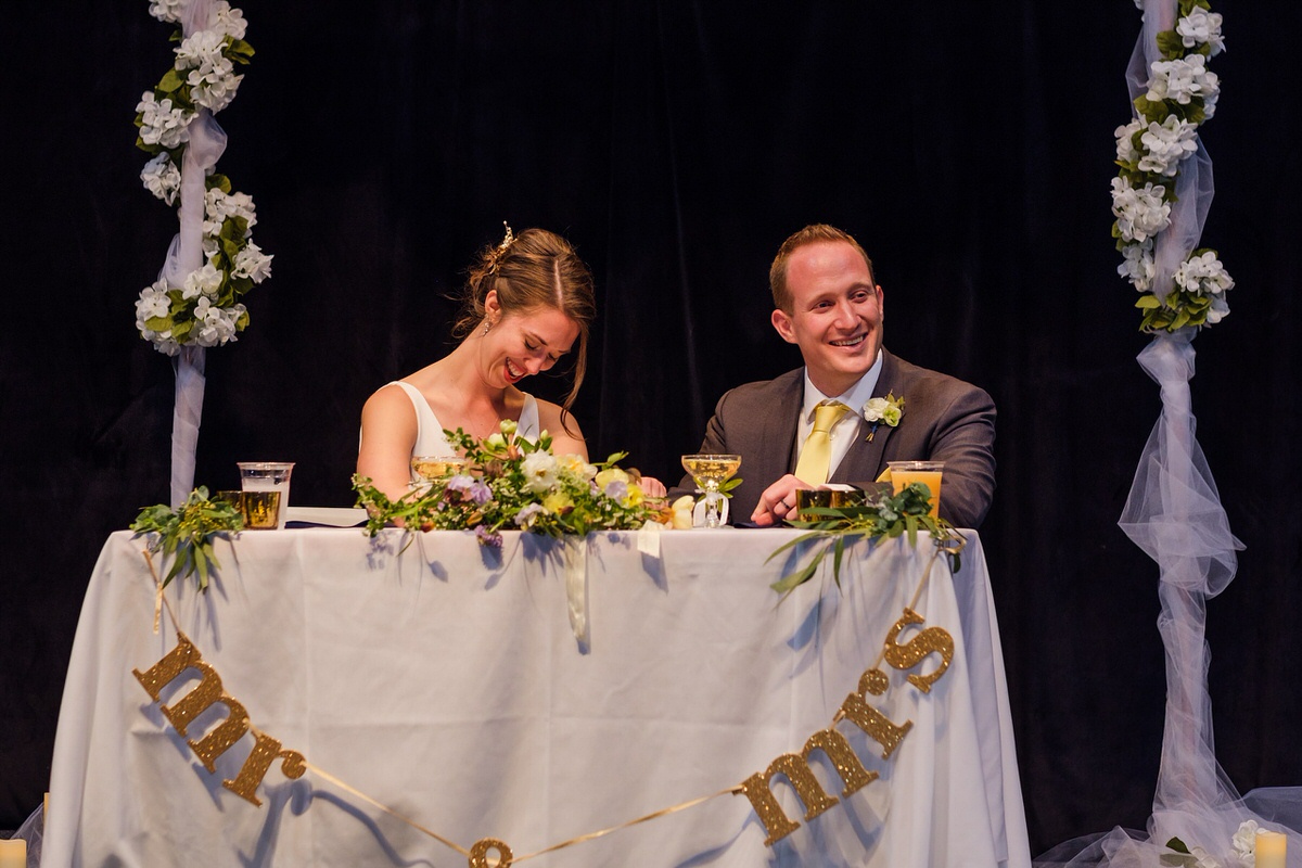 Bride and groom laugh from sweetheart table during toasts