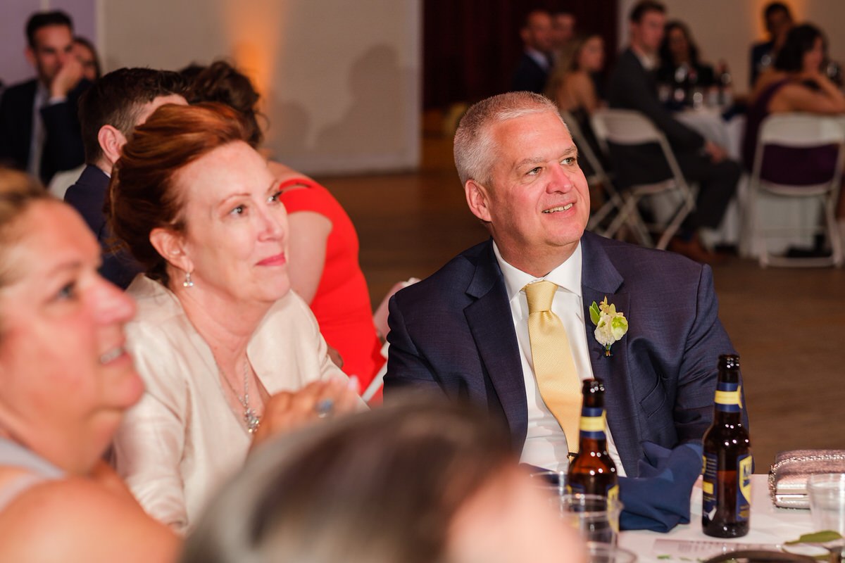 Bride's parents look on smiling during wedding toasts