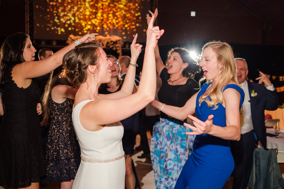 Bride raises her arms in the air while dancing with friends