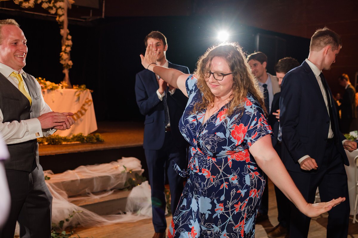 Wedding guest in a floral dress dances with arms spread wide like an airplane