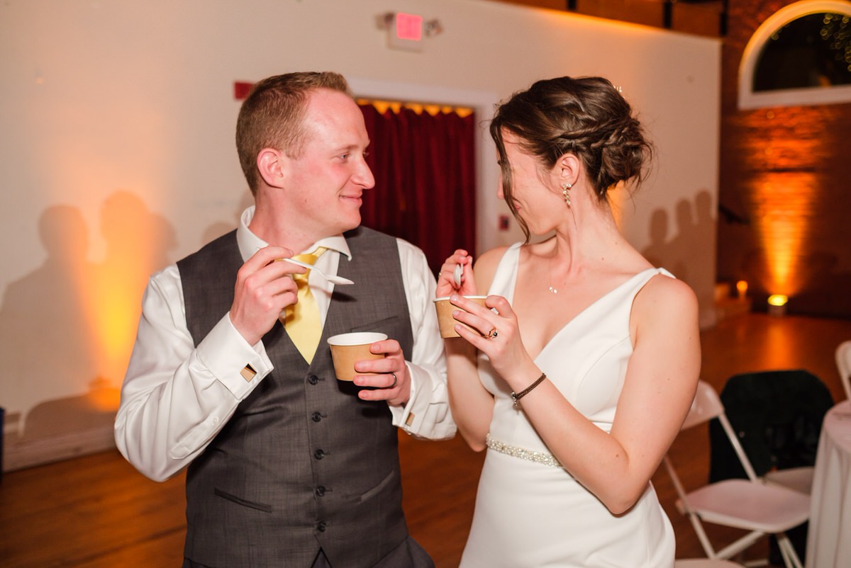 Bride and groom smirk at each other while eating ice cream