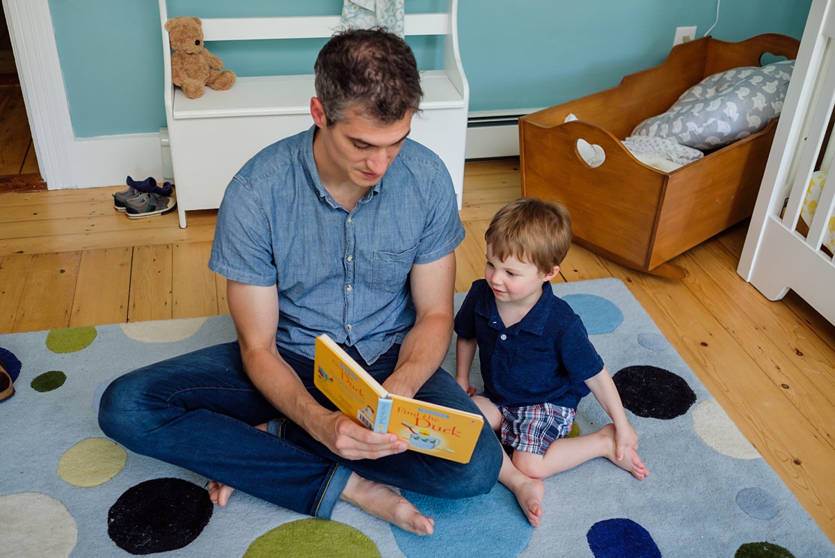 Father reads to his two year old toddle son on a blue rug