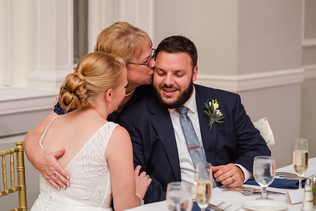 Groom's mom kisses his forehead while hugging bride