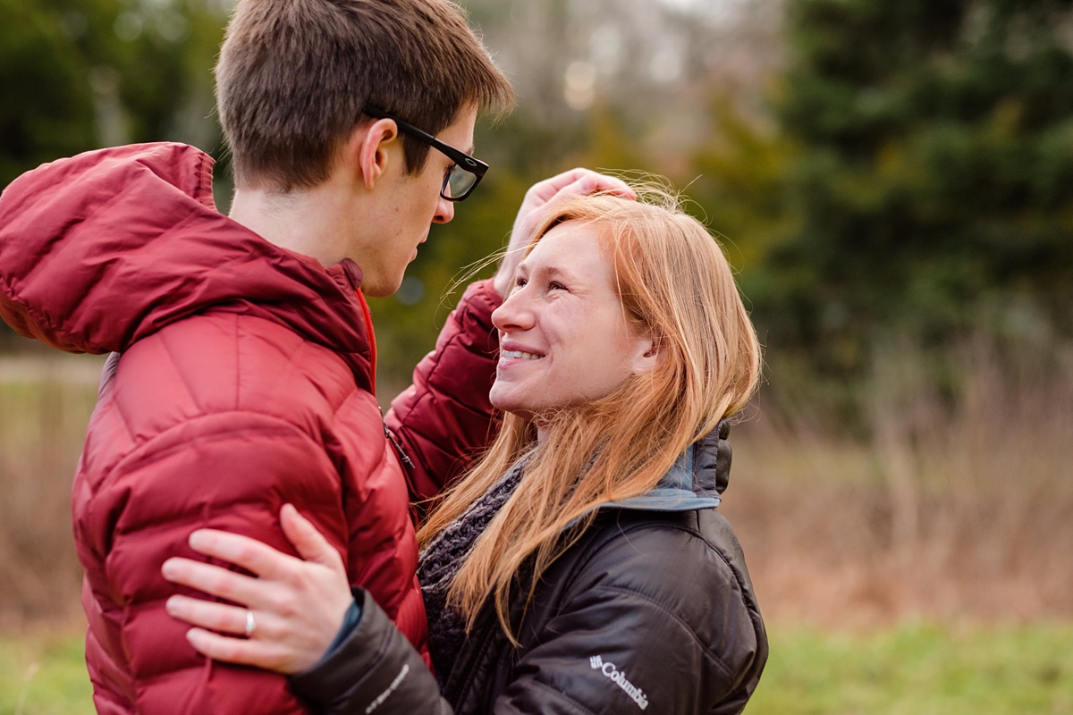 Man strokes his fiancee's hair in winter coats at a park in Boston