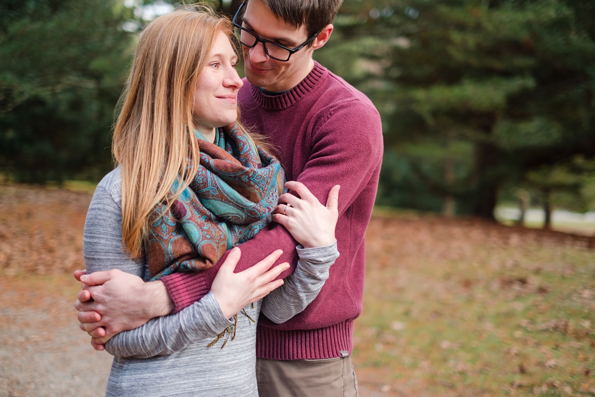 Woman gazes off while embraced by her fiance in engagement photos at the Arnold Arboretum in Boston