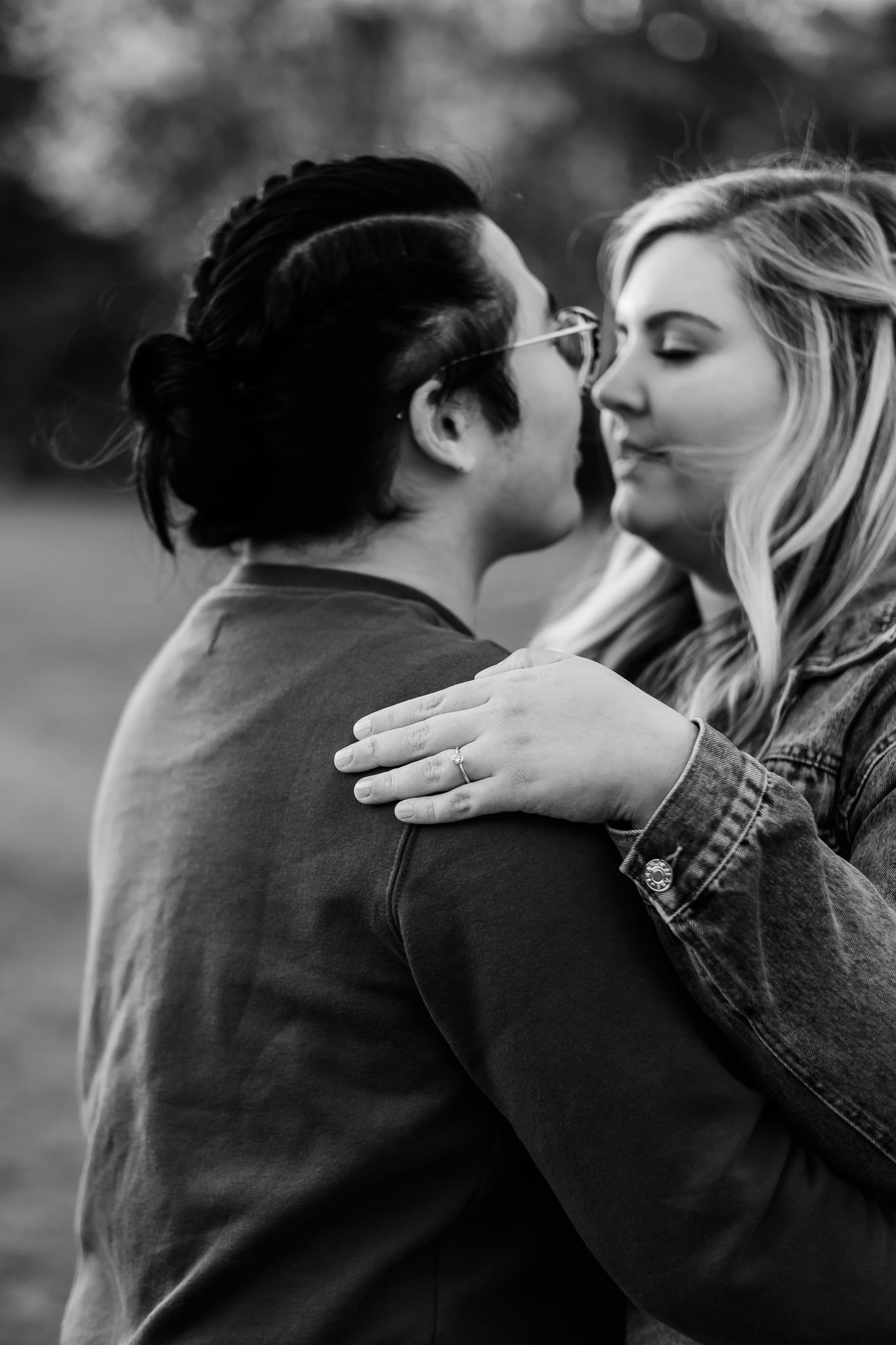 Engaged couple embraces with focus on woman's engagement ring on hand resting on man's shoulder