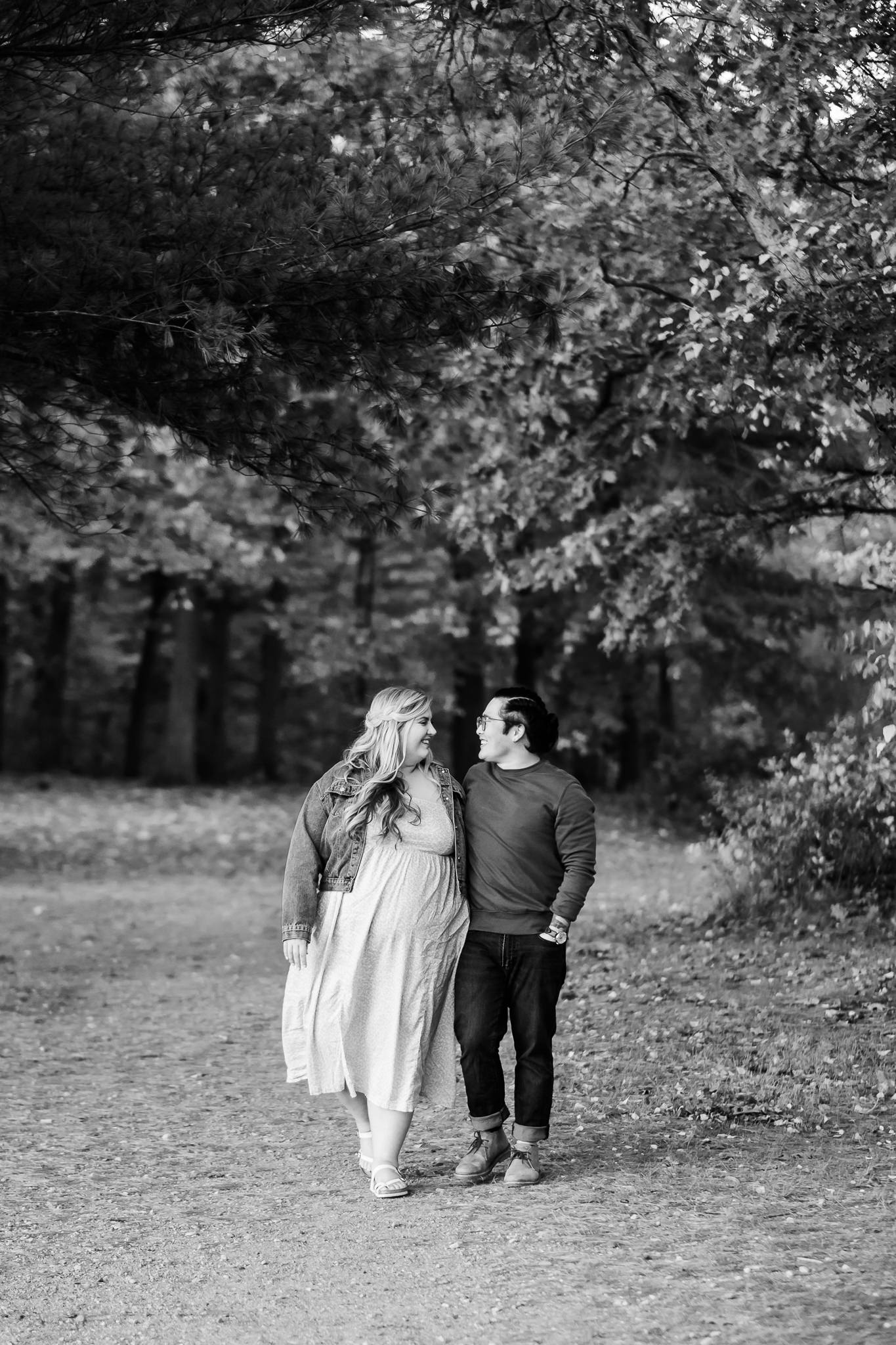 Engaged plus size blonde white woman and Asian man with a french braided faux hawk walk through the woods.