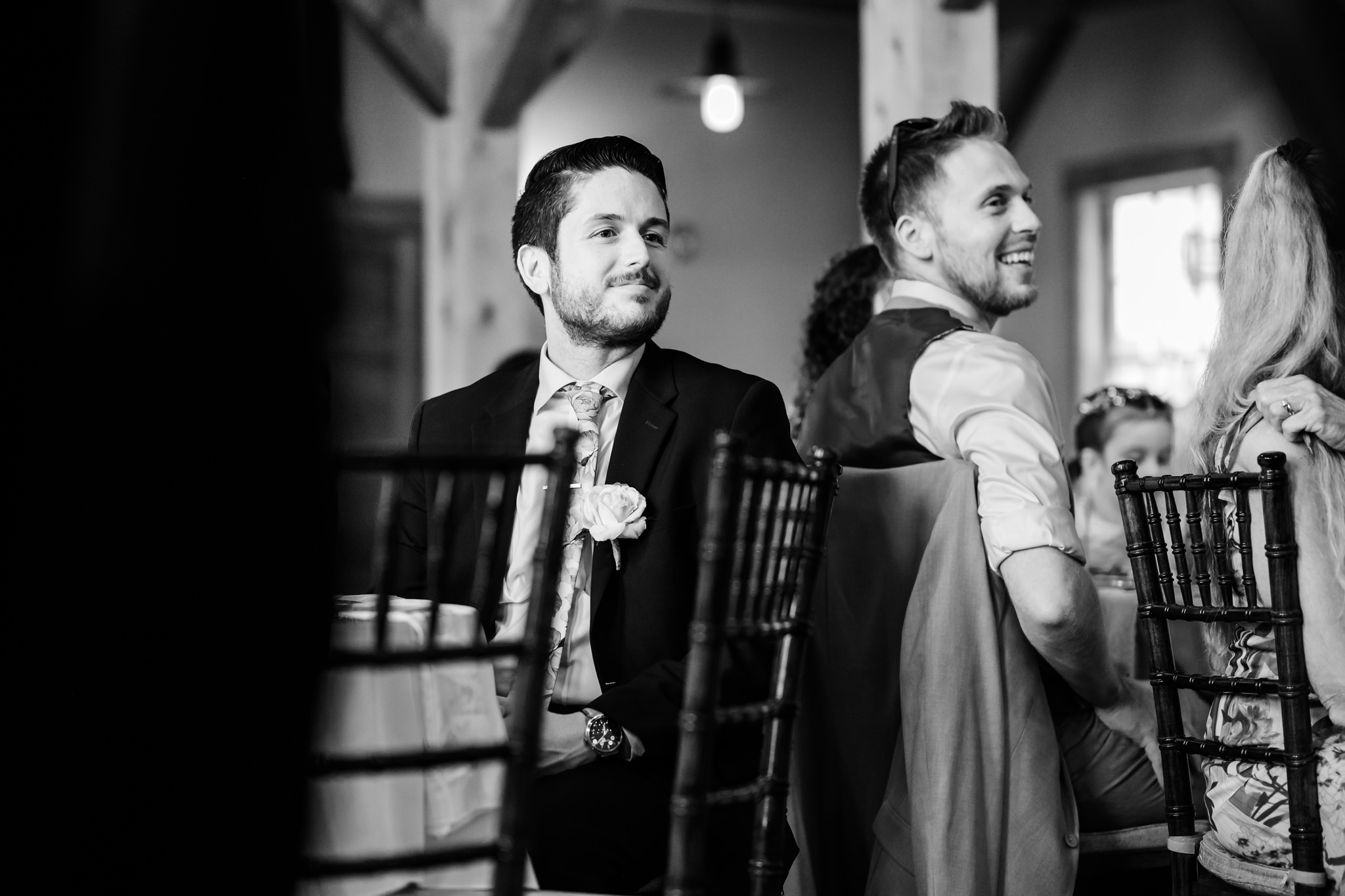 Seated guests in suits smile at Peirce Farm at Witch Hill wedding