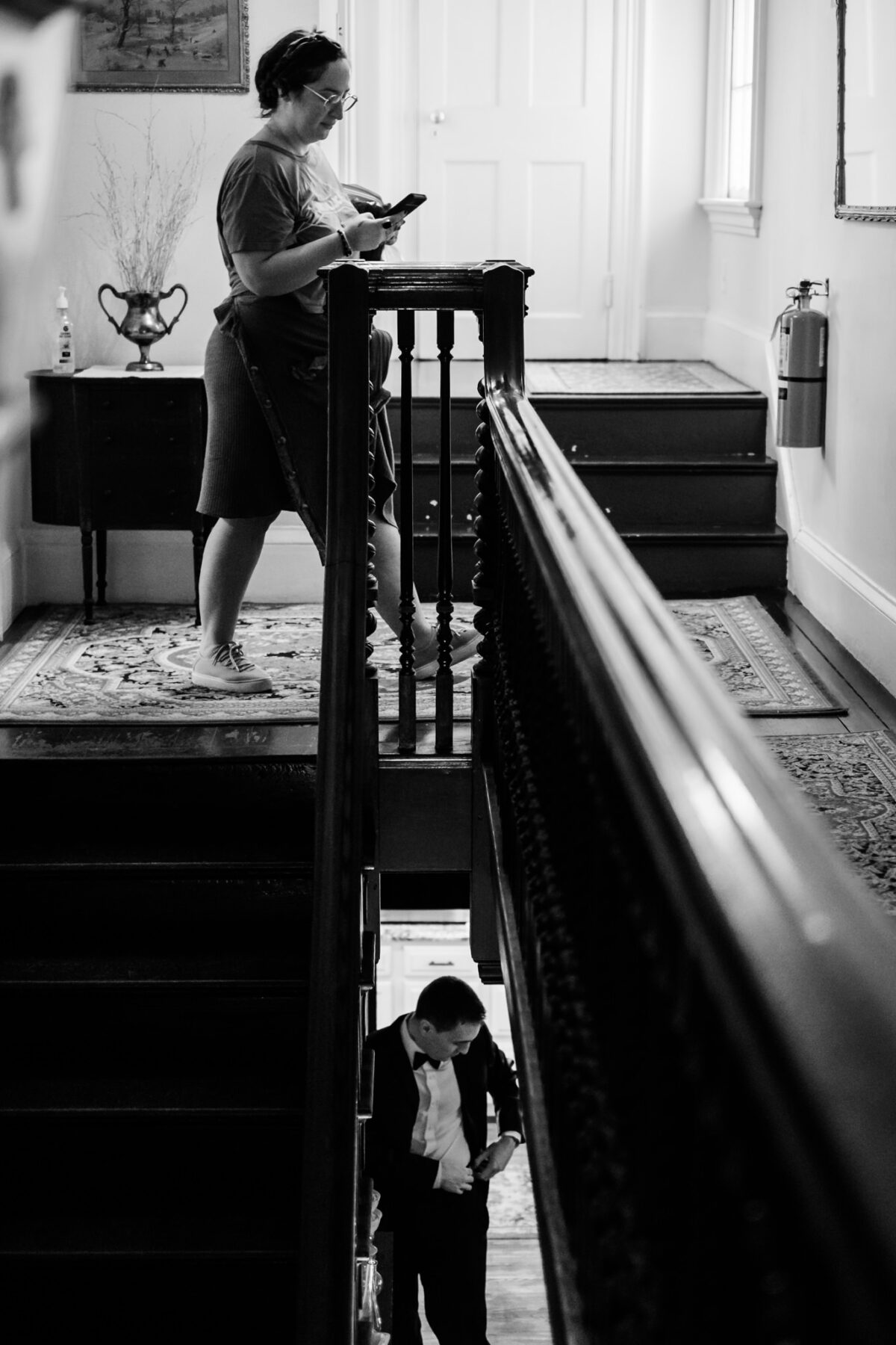 A bridesmaid in a tshirt walks upstairs and a groomsman tucking in his shirt is visible downstairs at Peirce Farm at Witch Hill