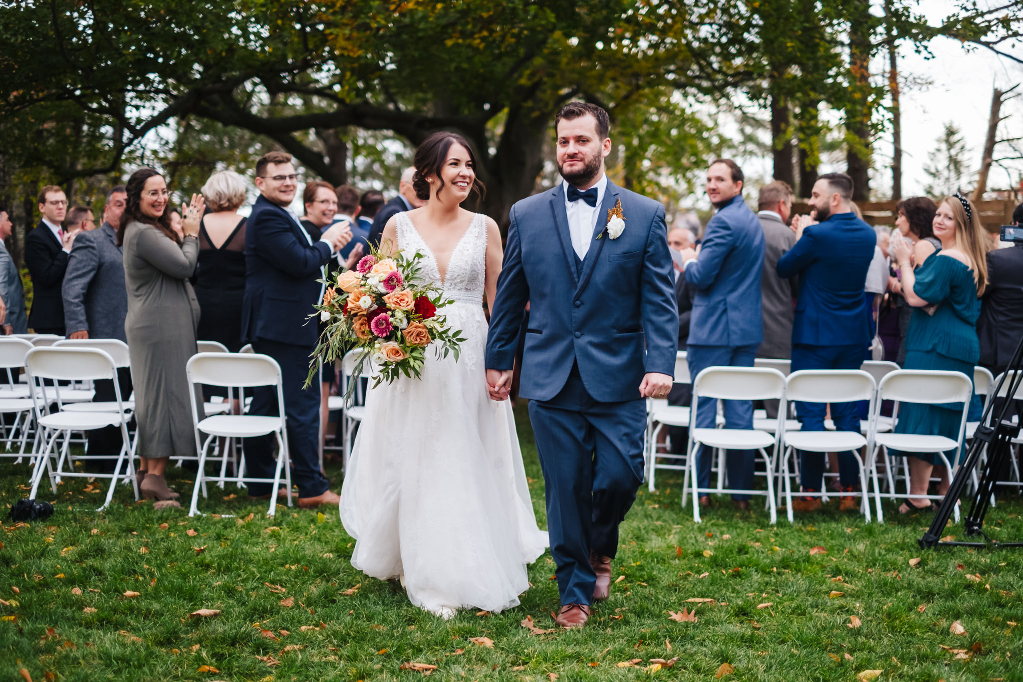 Bride and groom in navy suit recess down ceremony aisle as guests cheer